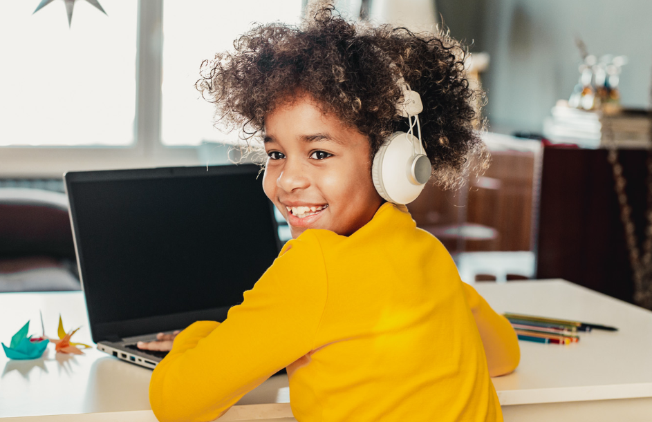 Happy child wearing headphones in front of a laptop.
