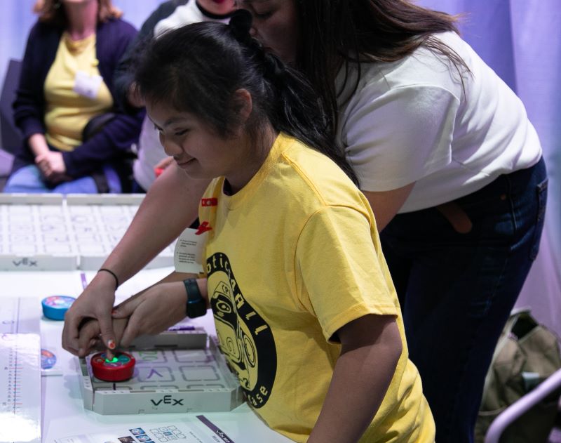 A blind student participates in a Vex programming activity with guidance from an adult